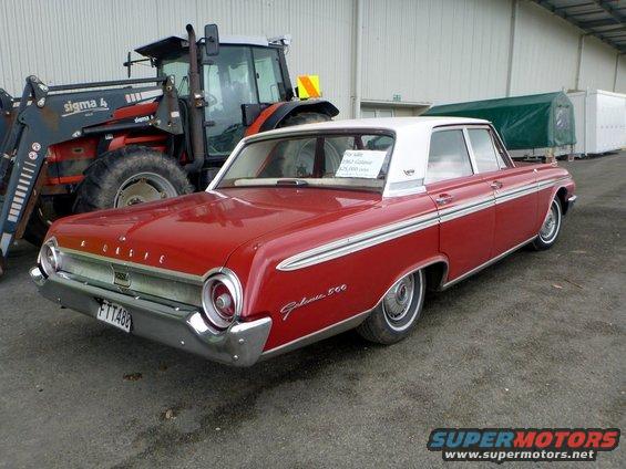 Red 1962 Ford Galaxie 500 sedan with white roof, parked next to a tractor