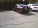 2003 Ford Crown Victoria - Maroon sedan with a large rear spoiler and aftermarket bumper damage is parked in a lot.