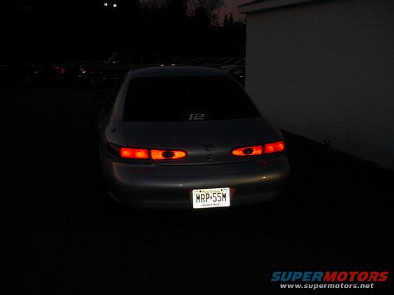 Rear view of a dark sedan with illuminated taillights and a license plate reading MRP-55M