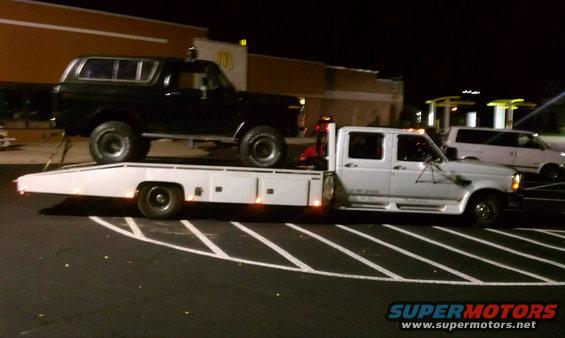 Black 1978 Ford Bronco on a flatbed tow truck at night