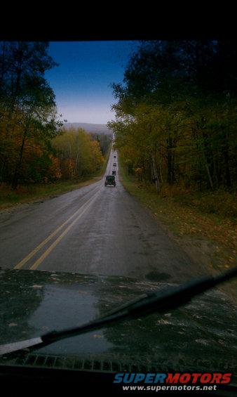 Several vehicles driving down a wet road lined with autumn trees