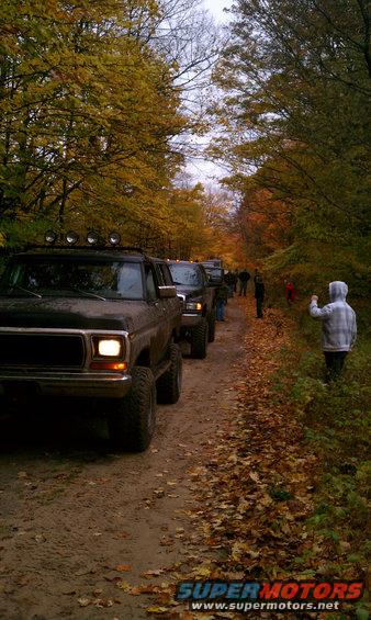 Front view of a 1979 Ford Bronco on a dirt road with fall foliage