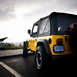 2004 Jeep TJ - A yellow 2004 Jeep TJ is parked outdoors, viewed from the rear, its soft top and off-road tires.