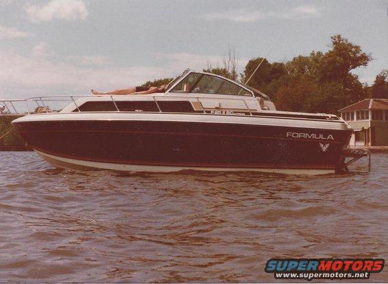 Dark blue and white Formula boat with a person sunbathing on deck, side view