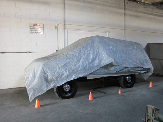 Vehicle covered in a tarp, parked indoors with orange cones around it