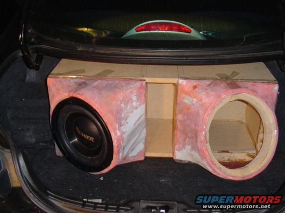 Car trunk with a custom-built subwoofer box. One speaker is installed, and there's an empty cutout for another