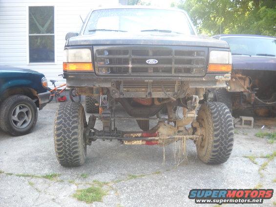 Front view of a 1992-1997 Ford F-Series truck with front bumper removed, showing suspension components. Another vehicle is parked to the left