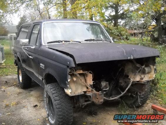 Black Ford Bronco with front end damage, missing grille and headlights. Off-road tires are visible