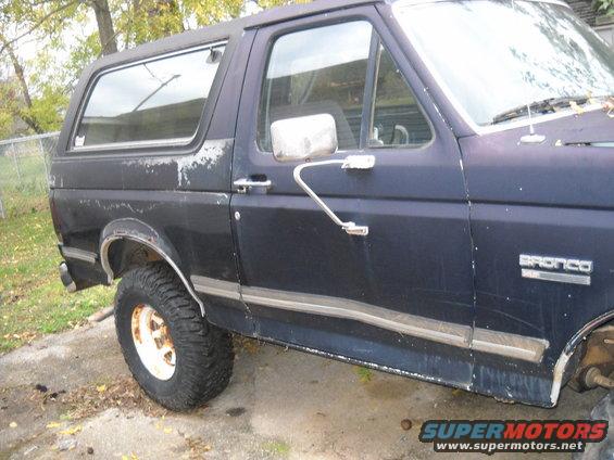 Dark blue 1982 Ford Bronco side view with peeling paint and white rims