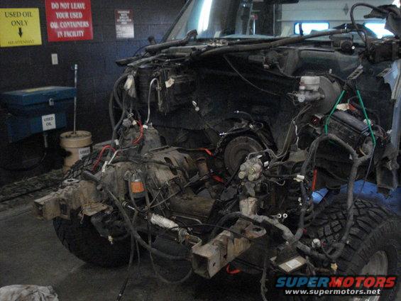 Disassembled vehicle chassis with exposed engine components and wiring, viewed from the front