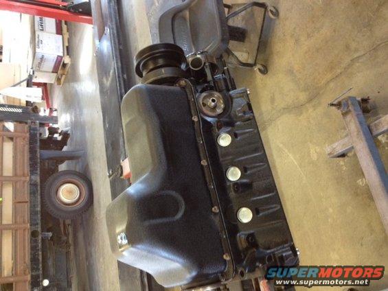 Black engine block with oil pan and pulley attached, resting on a shop floor