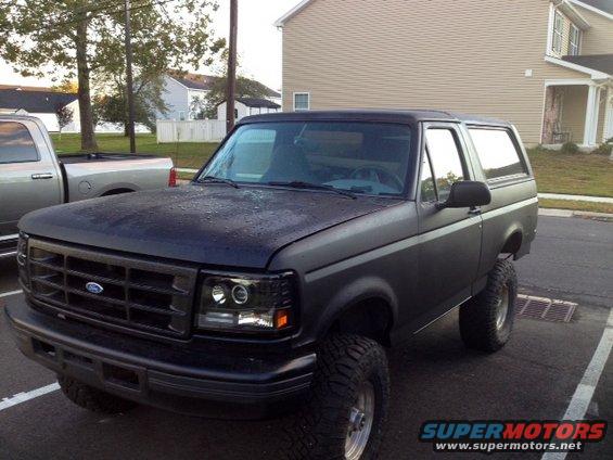 Dark matte Ford Bronco with lifted suspension and aftermarket headlights parked next to a silver pickup truck