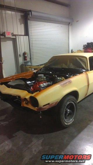 Car with hood open showing engine, in a garage. Body is yellow with primer spots