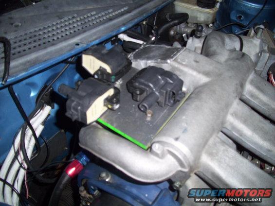 Engine bay showing three ignition coils mounted on a metal plate above intake manifold
