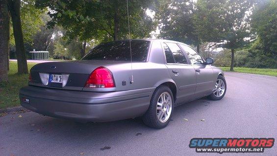Gray Ford Crown Victoria parked on a road with trees in the background. License plate is visible