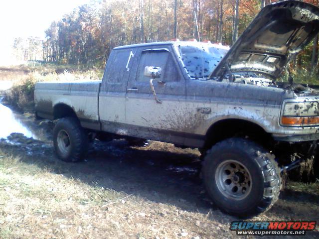 Muddy 1993 Ford F-150 with hood open, stuck in a muddy ditch