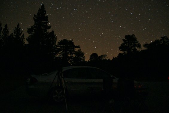 White sedan parked at night under a starry sky, with trees silhouetted against the sky