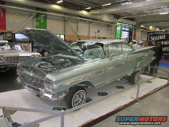Light blue 1959 Chevrolet Impala lowrider with hood open, parked next to another classic car