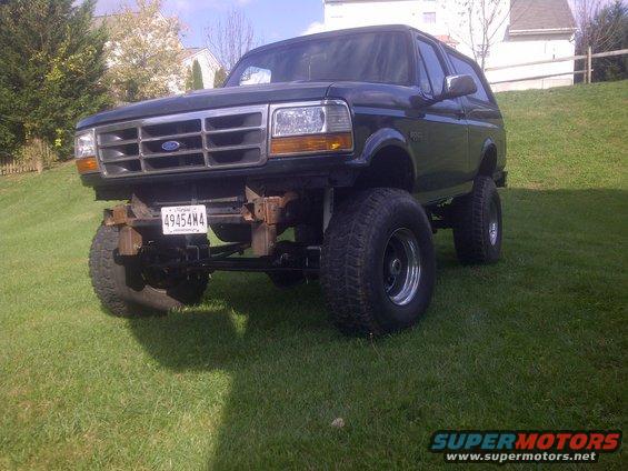 Lifted dark green Ford Bronco with aftermarket wheels and tires, parked on a grassy hill