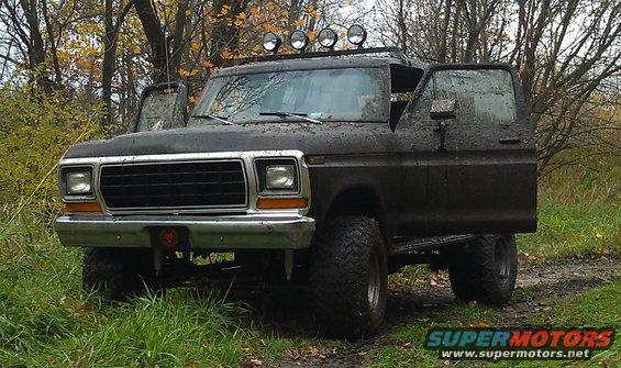 Mud-covered 1978 Ford Bronco with doors open, parked in a grassy, wooded area