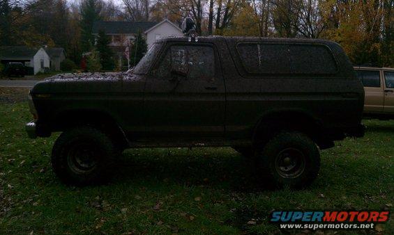 Mud-covered 1978 Ford Bronco side profile, parked on grass with another vehicle behind it