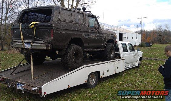 Mud-covered 1979 Ford Bronco on a flatbed tow truck, rear 3/4 view
