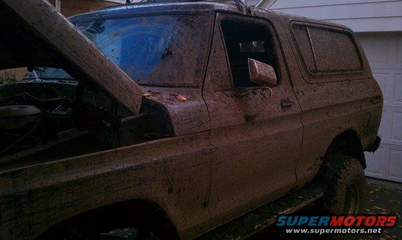 Mud-covered 1978 Ford Bronco with hood open, parked in front of a garage