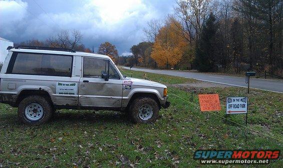 Silver SUV with "Kids in the Mudd" decal parked on grass near a road