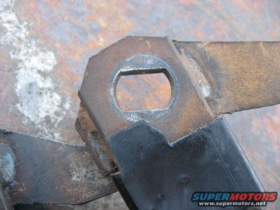 Close-up of a rusty metal bracket with a hexagonal opening, possibly part of a vehicle's drivetrain or suspension