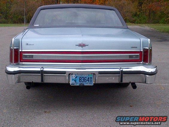 Rear view of a light-colored sedan with a chrome bumper and a blue license plate