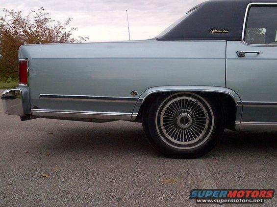 Light blue Lincoln Continental with a black vinyl roof, seen from the rear quarter, showing a wire wheel and chrome trim