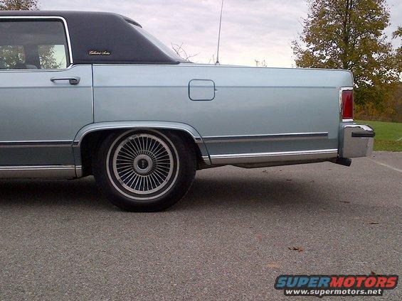 Light blue sedan with black vinyl roof, rear quarter panel, and wire wheels