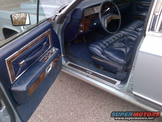 Interior of a light blue Lincoln Continental with plush blue leather seats and wood trim on the door panel