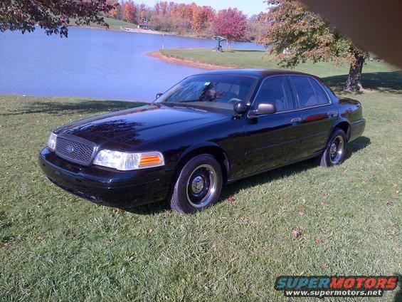 Black 2001 Ford Crown Victoria parked on grass near a lake with autumn trees