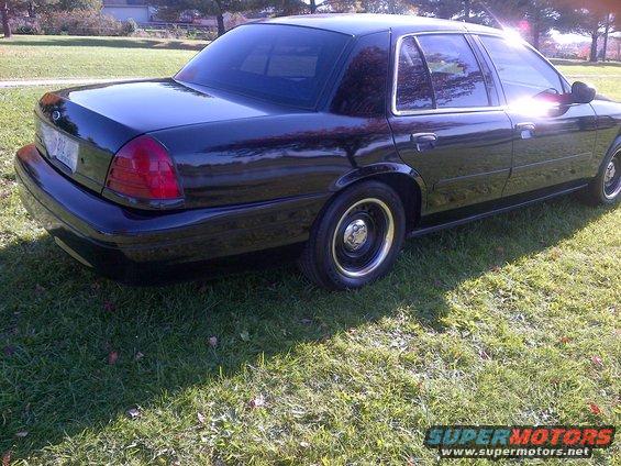 Black sedan parked on grass, showing rear quarter panel and side profile. Tinted windows and chrome trim visible