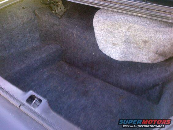 Car trunk with dark carpet and a spare tire. Supermotors.net logo visible