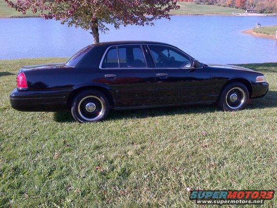 Side view of a black 2001 Ford Crown Victoria parked on grass by a lake