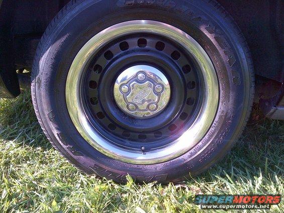 Black steel wheel with chrome trim and Ford hubcap on grassy ground