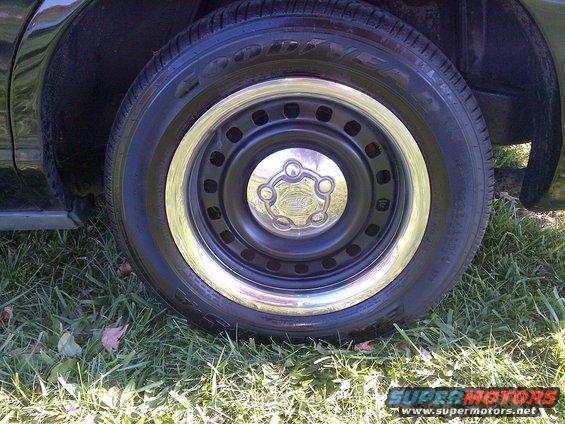 Close-up of a steel wheel with a chrome trim ring and hubcap on a tire. Grass and leaves are visible below