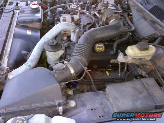 Engine bay with air intake, radiator hoses, and engine cover visible. Supermotors.net logo in lower right
