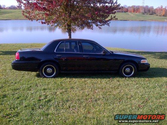Black 2001 Ford Crown Victoria sedan, side view, parked on grass by a lake