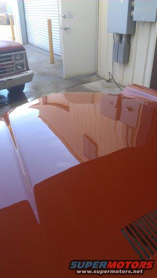 Orange car hood reflecting a building and a red truck