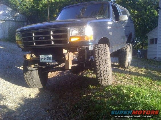 Dark blue Ford Bronco with lifted suspension, missing front bumper, and off-road tires