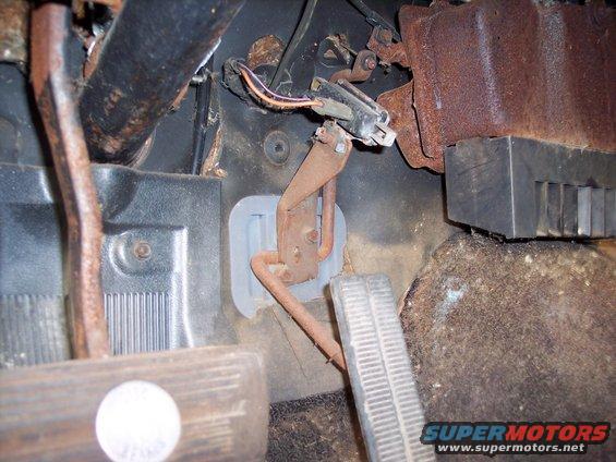 Close-up of rusty brake and clutch pedals, wiring, and firewall in a vehicle interior