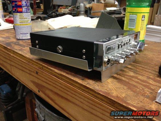 CB radio with knobs and a digital display on a wooden workbench, next to a can of spray and a green bottle