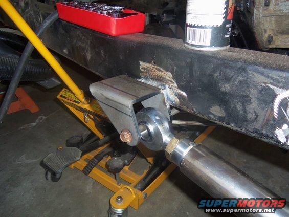 Vehicle frame with custom bracket and suspension component attached, supported by a yellow jack