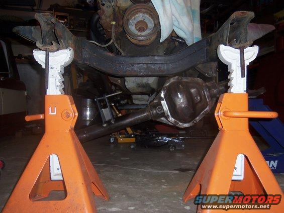 Vehicle frame and differential supported by orange jack stands, with engine components visible above