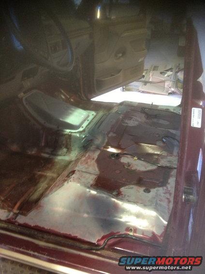 Interior of a vehicle with seats removed, showing bare metal floor and some reddish staining