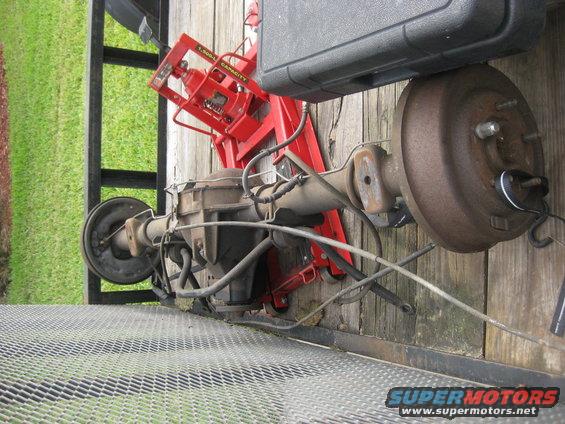 Rear axle assembly with drum brakes, supported by a red jack on a wooden surface
