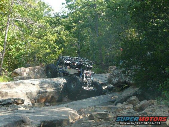 Custom off-road buggy navigating a rocky trail with trees in the background